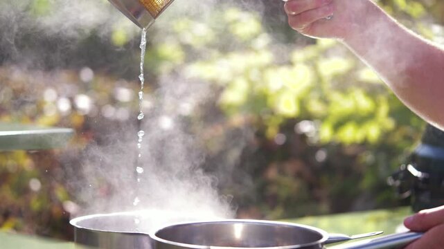 Hands pour honey over golden honeycomb into a stainless steel pan