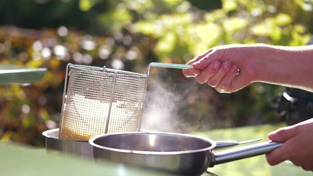 Hands strain pasta through a mesh sieve over a pot outdoors