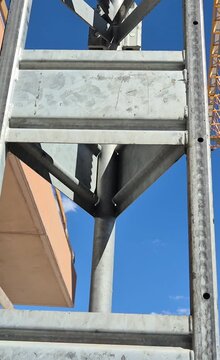 Vertical 9:16 aspect ratio shot of an industrial personnel hoist moving up a lattice mast as a tower crane jib turns over the building under construction.