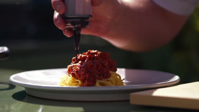 Chef plates spaghetti with rich meat sauce on a white plate