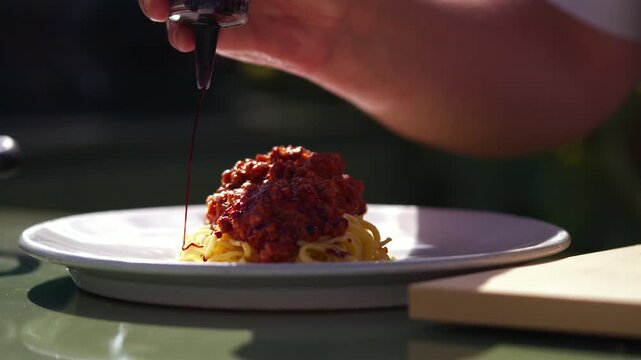 Chef plates spaghetti with meat sauce in a dark outdoor kitchen setting