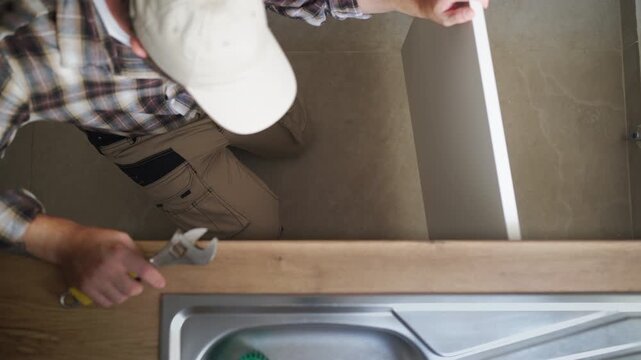 Skilled plumber using an adjustable wrench to repair a sink pipe in a modern kitchen, demonstrating professional craftsmanship, technical expertise and home maintenance work.