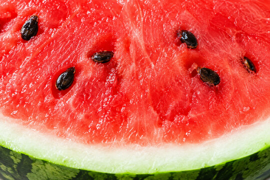 Close-up of the cut surface of a fresh red watermelon with black seeds and green rind in bright light