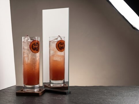 Tall cocktail glass reflected beside mirror on dark countertop