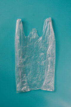 Used transparent plastic shopping bag lying flat on a blue background, representing disposable packaging and plastic waste