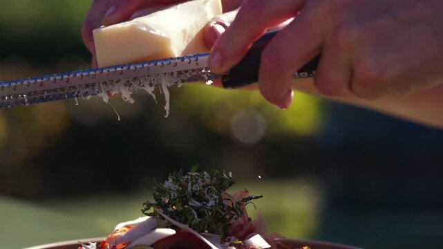 Chef grates Parmesan cheese over a gourmet dish in an outdoor kitchen