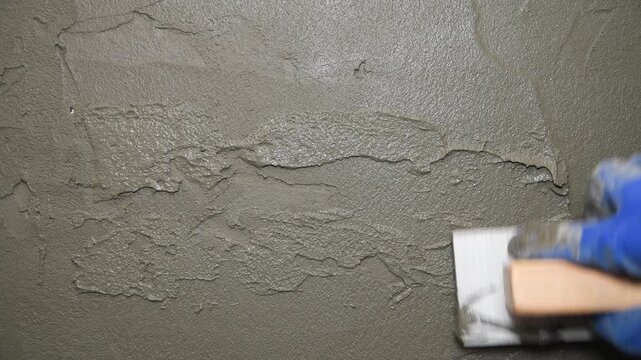 Worker creates unevenness in the plaster to imitate antiquity using a float. Repair plastering works.