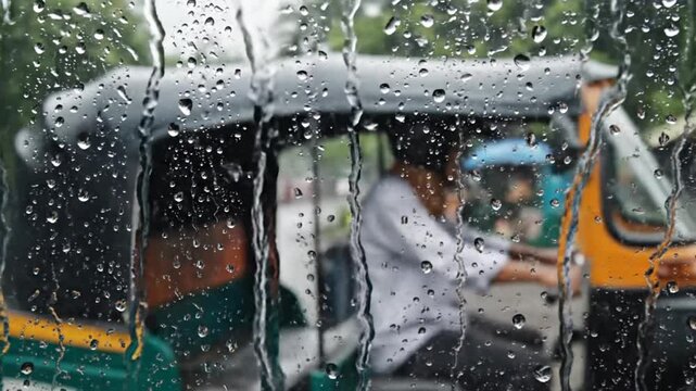 Auto rickshaw tuk tuk driving on street seen through glass with rain drops. Monsoon rain in India, rainy day transit, urban transportation, weather storm, and asian street life concept. 
