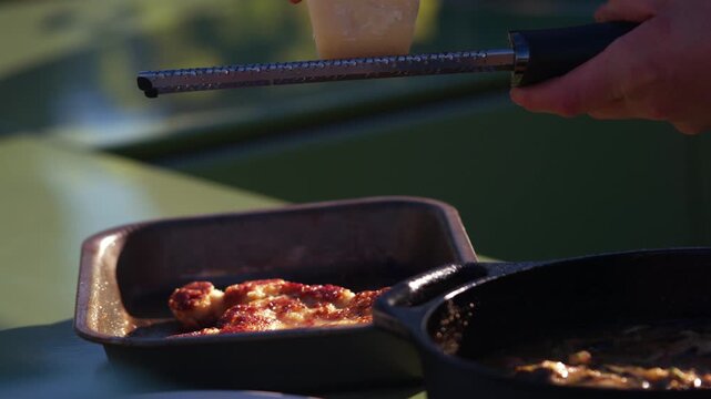 Parmesan cheese is freshly grated over a savory dish outdoors
