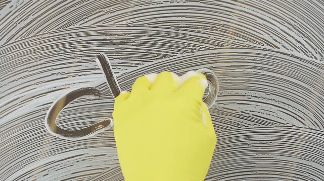 A person is using a yellow cleaning cloth to wipe a surface in a pattern. The word clean is formed visibly as the surface is wiped with the cloth.
