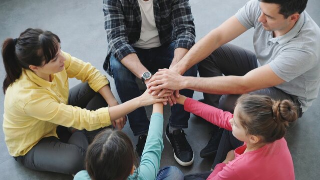 Group of people sitting in circle joining hands for teamwork and unity