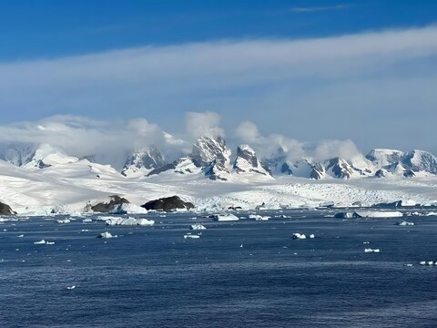 Antarctic landscape with rugged snow-capped mountains and floating icebergs in deep blue water under a cloudy sky
