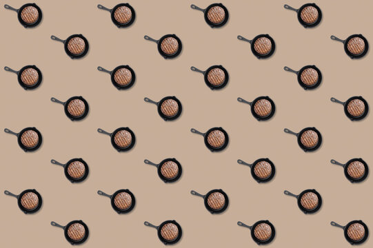 Small black skillets with grilled burger patties repeated in diagonal rows across a beige food pattern background