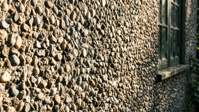 Exterior building wall covered in embedded smooth river stones illuminated by warm golden hour sunlight
