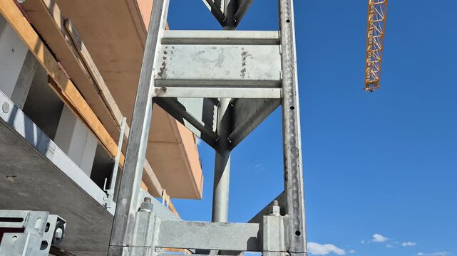 Slow motion shot of an industrial personnel hoist ascending a lattice mast on a residential building under construction as a tower crane jib rotates.
