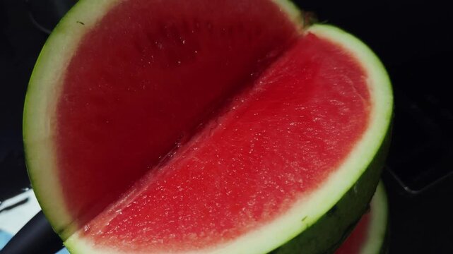 Red watermelon flesh fills close view as cut half rests against dark setting. Fresh fruit has moist, appetizing surface and contrasting green rind, suggesting summer refreshment. Green skin borders