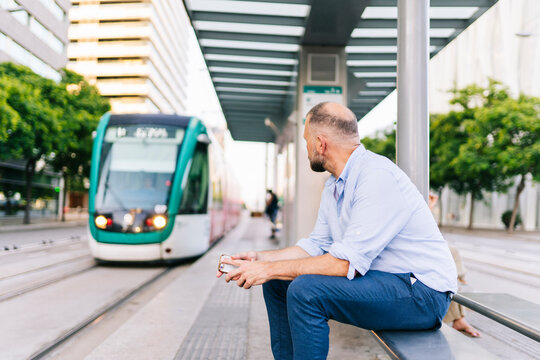 Man waiting for tram at city stop holding phone