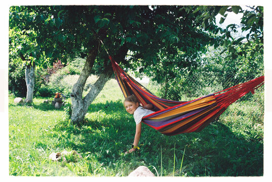 Girl leaning out of a colorful hammock under trees in the garden
