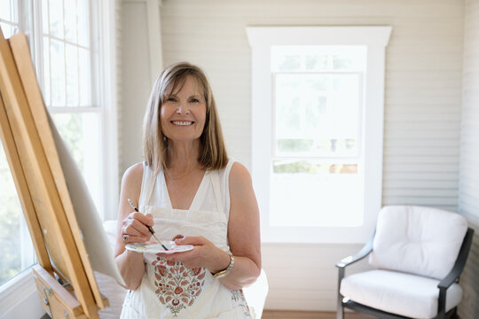 Smiling woman artist painting on easel in bright home studio