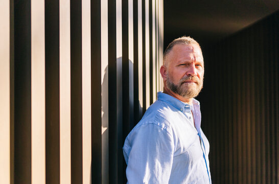 Middle aged man with beard standing by striped wall