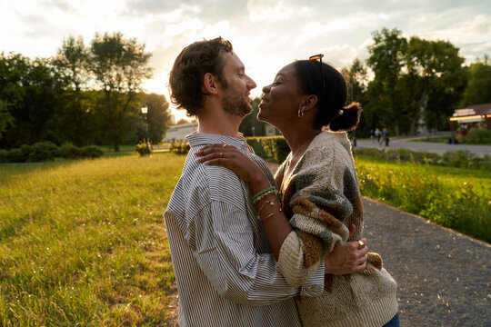 Diverse couple hugging and looking at each other in park