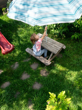 Young girl in denim overalls  opens the umbrella on a picnic table