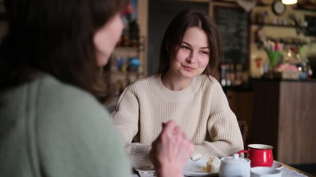 Beautiful young daughter listening carefully to her mother's advice during a heartfelt and emotional conversation, sitting together at a cozy cafe table and sharing a special family moment