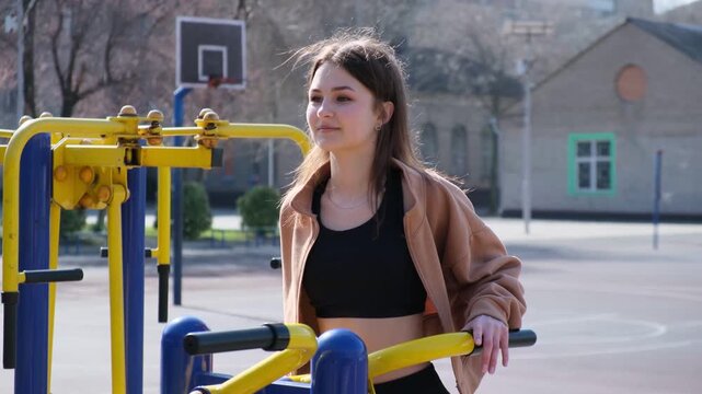 Fit young woman performing triceps dips on parallel bars at an outdoor sports ground, improving her strength and endurance with a focused expression during her calisthenics workout