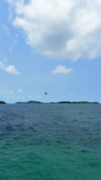 Tropical Sea with Distant Parasailing, Islands and Blue Sky. Wide tropical seascape with distant parasailing, turquoise water, small islands and blue sky with copy space.
