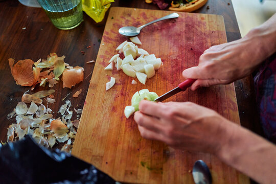 Hands Chopping an Onion on a Wooden Cutting Board in a Kitchen
