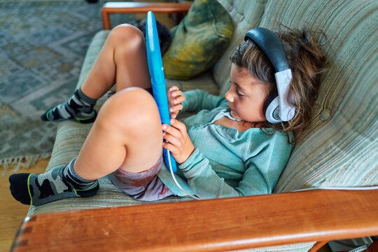Boy With a Tablet and Headphones Lounging on a Green Sofa