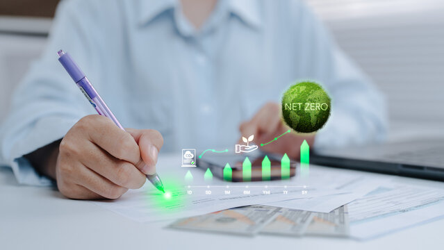 Person planning net zero and green business sustainability strategy, writing notes on financial documents with glowing earth globe and carbon reduction growth charts.