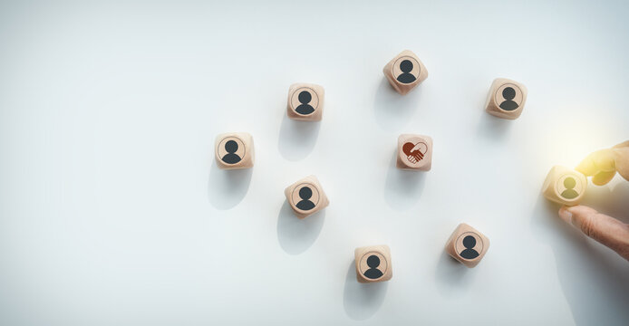 Hand placing a wooden block with a human icon among network blocks with a partnership symbol on a white desk, concept of human resource management, networking, and business collaboration.