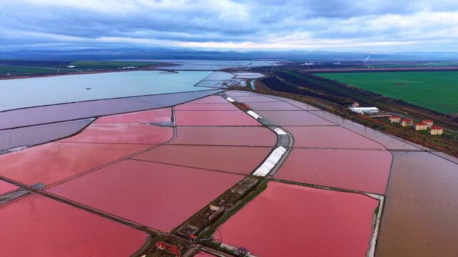 Salt pans with various colors in a landscape with water and fields. Salt pans show different shades of color during the day in a rural area.