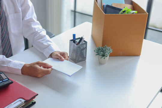 Office worker handing over an envelope, next to a packing box filled with personal belongings. Concept for resignation or leaving a job.