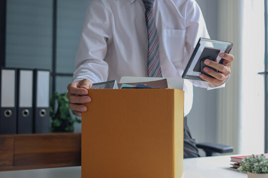 Businessman packing personal belongings in cardboard box after being fired.