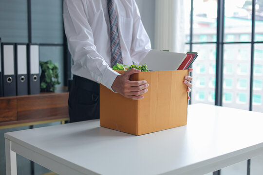 Businessman holding cardboard box with office supplies after resigning from job.