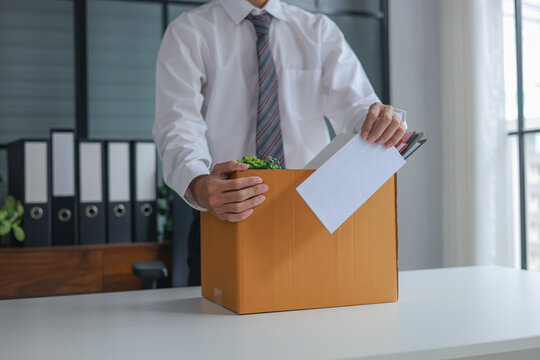 Business professional holding resignation letter and packed of personal belongings in cardboard on a desk. Concept of job resignation or termination.