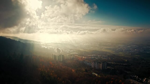 Aerial nature shot with sunbeams and layers of dramatic clouds in the sky over a European town surrounded by woodlands.