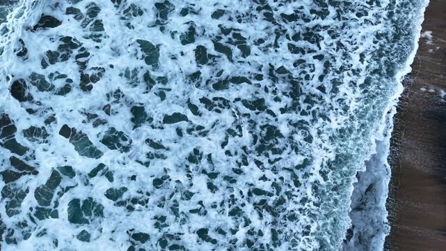Waves crashing on a beach during daylight. Waves roll onto the shore, mixing with sand in bright daylight.