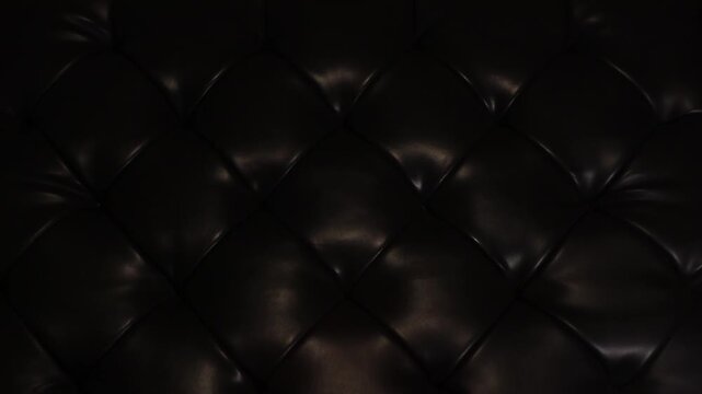 Close-up shot of a light streak sweeping across a tufted black leather surface for background or titles