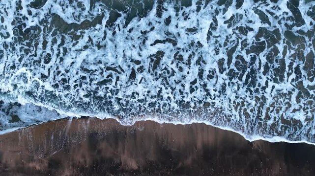 Waves crash on a sandy beach during daylight on the shore. Waves roll onto a sandy beach under bright sunlight with no people present.