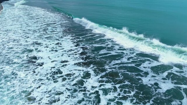 Ocean waves crash on shore under bright sky near coast. Waves move toward the shoreline along a coast with clear water and blue sky.