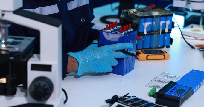 Forensic technician in blue gloves examines a small electronic device beside a microscope and evidence tools in a modern laboratory.