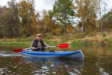 Man paddling a blue kayak with a red paddle on a river in autumn forest © WoodHunt