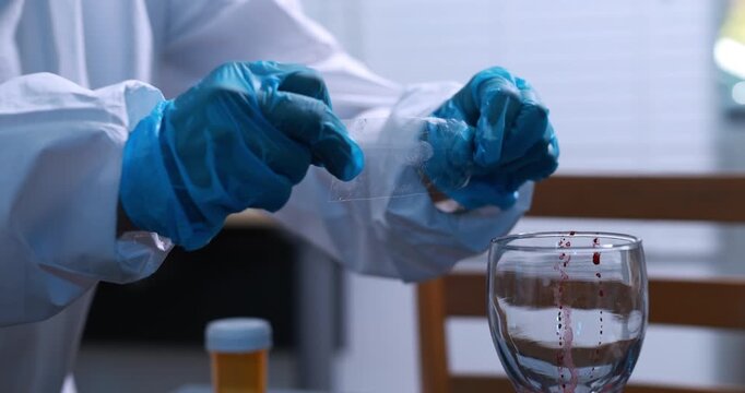 Close-up of a laboratory worker in blue gloves handling a blood sample above a glass, medical testing, forensic analysis, and hygiene.