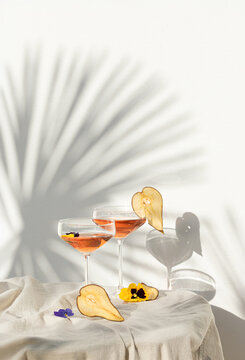 Two rose wine glasses with summer cocktails and dried fruit appetizers. Tropical light background with palm shadow.