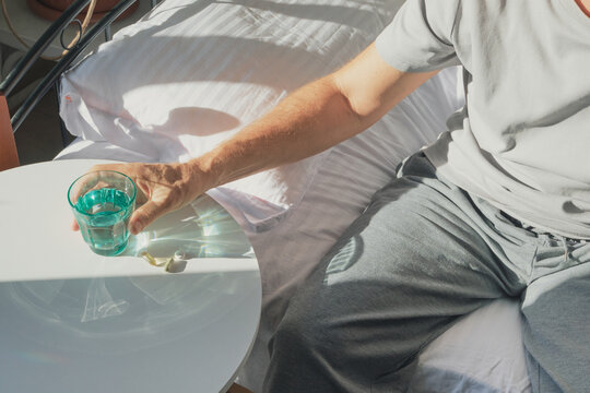 Man reaching for glass of water and pills while resting in bed