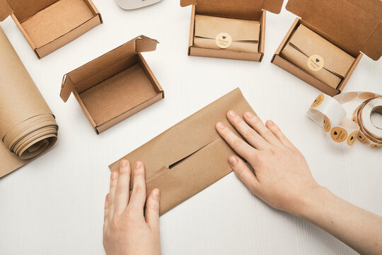 Female Hands folding brown paper around package with cardboard boxes and thank you stickers on white table