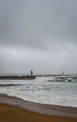 Fototapeta premium Stormy Atlantic ocean with powerful waves hitting coastline in Porto Portugal. Dramatic seascape with dark clouds, rough sea and coastal pier during bad weather conditions.